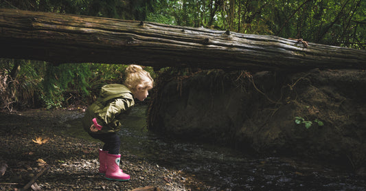 Girl wearing welly boots looks at tree roots